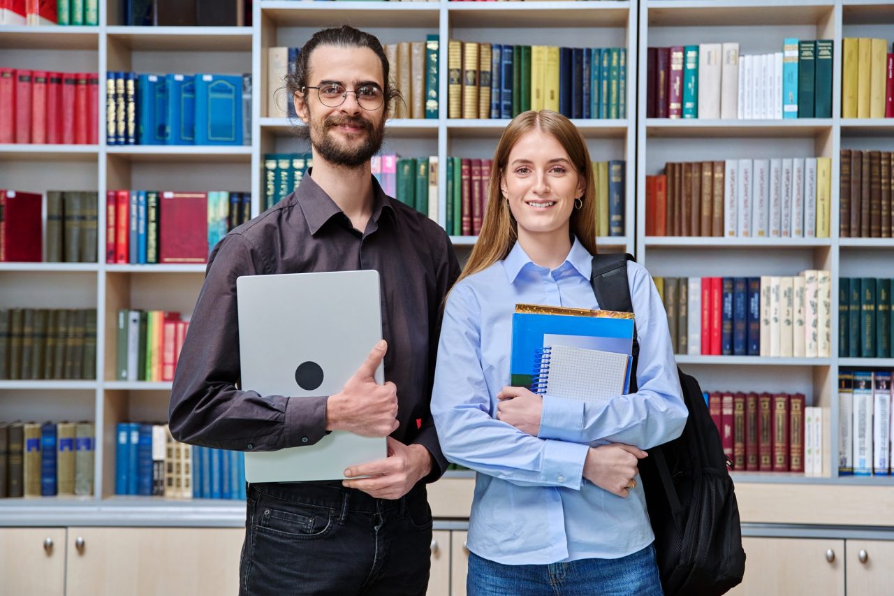portrait of young male teacher and teenage girl student looking at camera in college library.jpg